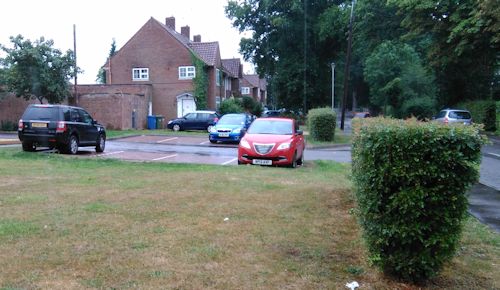 Archive photograph of a neighbourhood parking area beside homes and a green space